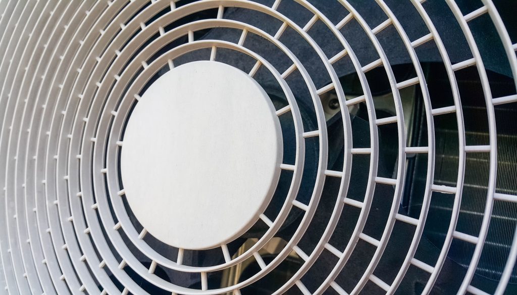 Nahaufnahme des Ventilatorgitters einer Wärmepumpe mit kreisförmiger Struktur und sichtbaren Lüfterblättern.