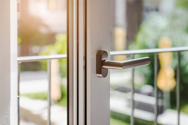 Geöffnetes Fenster mit Metallgriff und Sonnenlicht im Hintergrund.