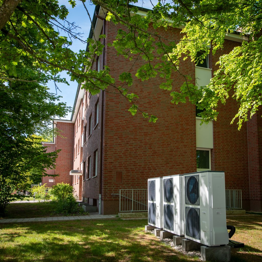 Mehrfamilienhaus aus rotem Klinker mit außen aufgestellter Wärmepumpenanlage im begrünten Innenhof.