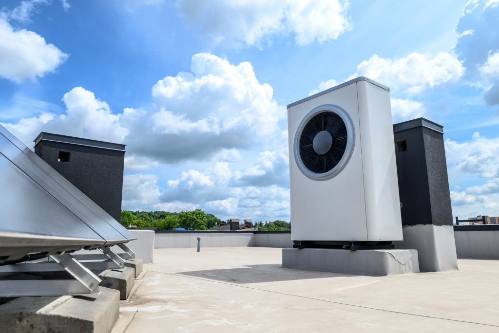 Außeneinheit einer Wärmepumpe auf einem Flachdach bei blauem Himmel.