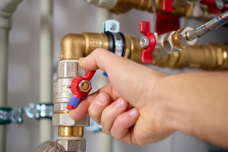 Jemand stellt ein Ventil an der Wärmepumpen-Rohrleitungsanlage mit Rohren und Verbindungsstücken manuell ein.