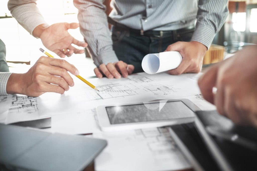 Drei Kollegen arbeiten im team an technischen Zeichnungen, die auf dem Tisch liegen